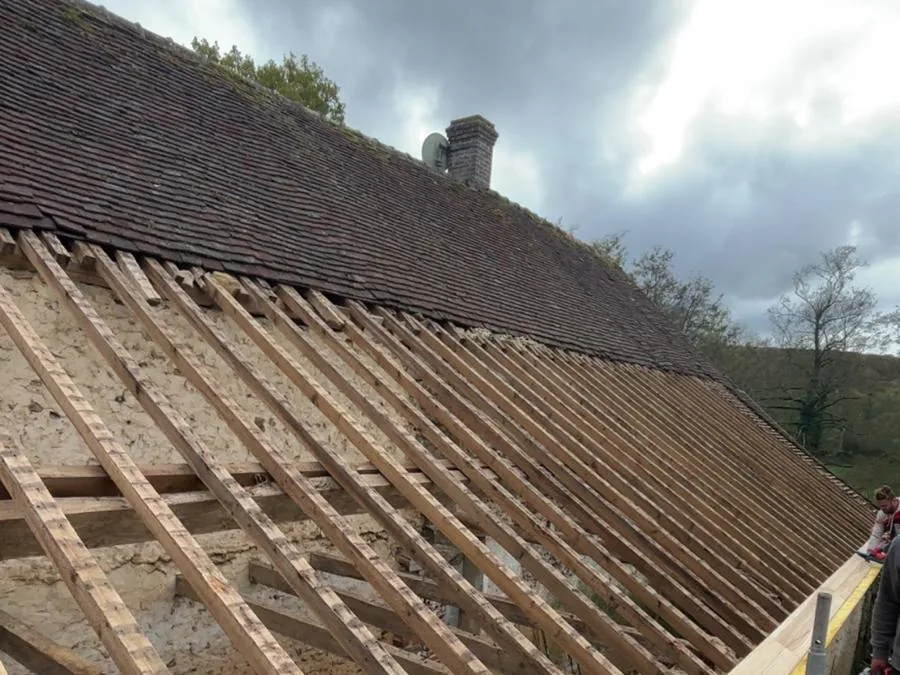 Dépose de l'ancienne couverture d'une longère : chevrons mis à nu au-dessus d'un mur en silex