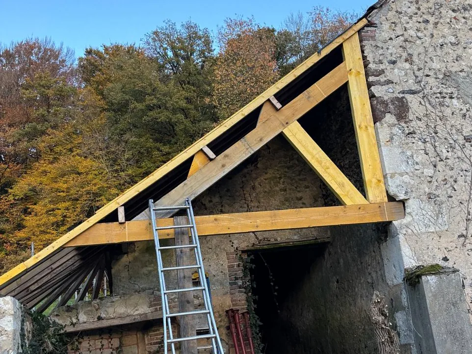 Ferme de charpente neuve en bois posée sur le pignon en silex d'une longère