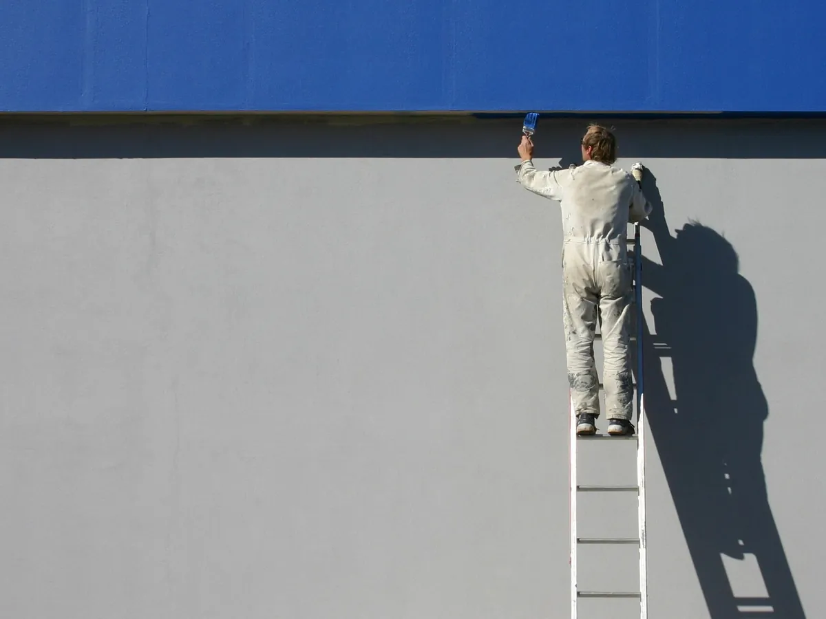 Peintre en bâtiment sur une échelle appliquant une peinture sur une façade